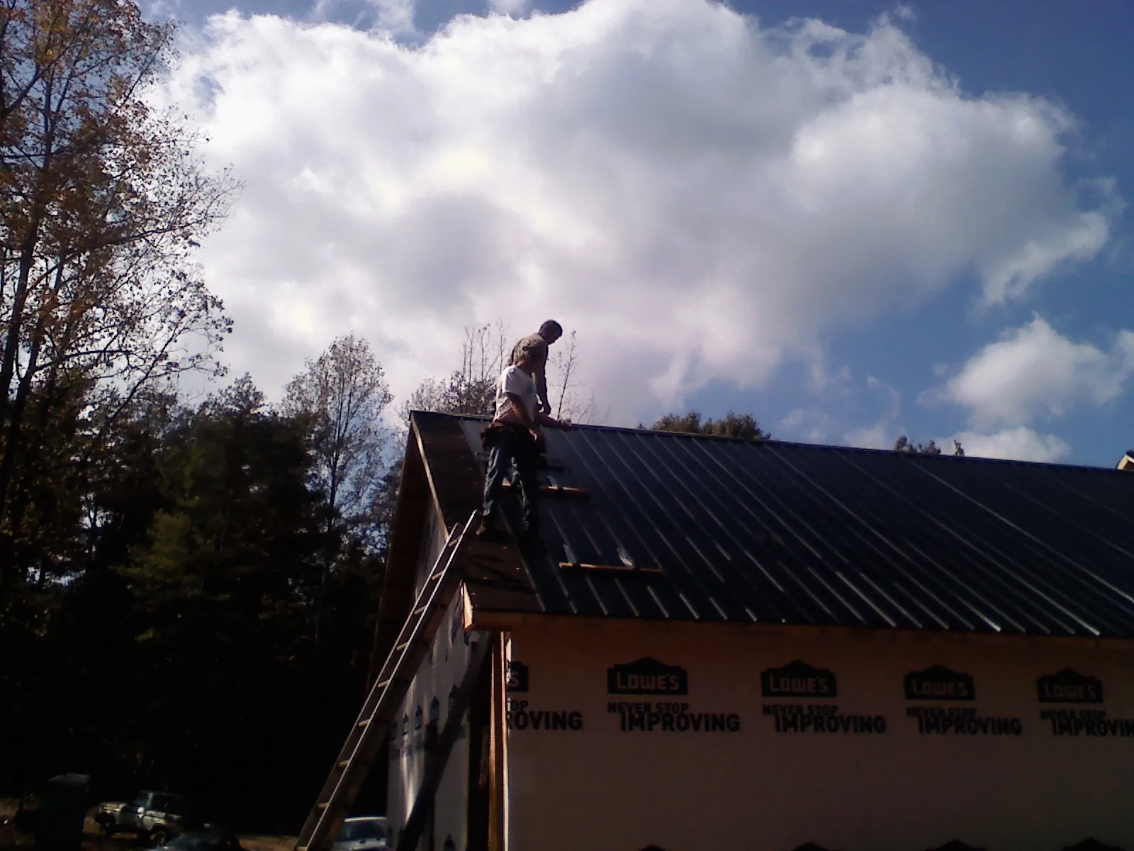Roofer fastening dark metal panels high against a cloudy sky, from a Roof Inspection job in Waukegan