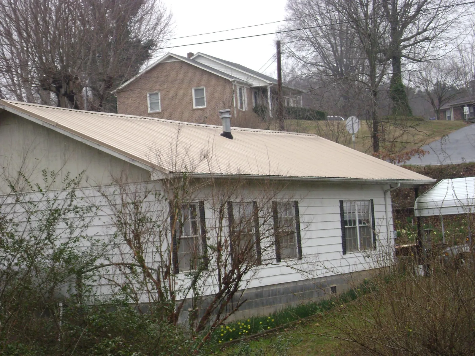 Tan metal roof on a white sided house set into a hillside — Commercial Roofing by Roofing Brothers in Waukegan